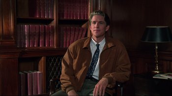 Movie still from “Gross Anatomy” (1989), directed by Thom Eberhardt – A man sitting in front of a book shelf; Medium shot, High angle