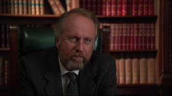 Movie still from “Gross Anatomy” (1989), directed by Thom Eberhardt – A man in a suit and tie sitting in front of a book shelf; Close Up shot, Low angle