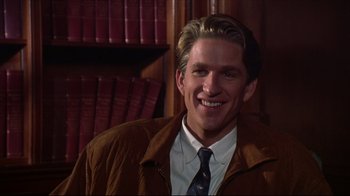 Movie still from “Gross Anatomy” (1989), directed by Thom Eberhardt – A man in a suit and tie smiling for the camera; Close Up shot, Over the shoulder angle