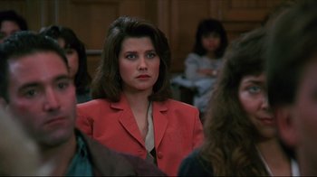 Movie still from “Gross Anatomy” (1989), directed by Thom Eberhardt – A woman in a red jacket in a court room; Close Up shot, Over the shoulder angle