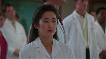 Movie still from “Gross Anatomy” (1989), directed by Thom Eberhardt – A woman in a white lab coat is standing in front of a group of people; Close Up shot, Low angle