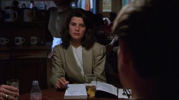Movie still from “Gross Anatomy” (1989), directed by Thom Eberhardt – A woman sitting at a table in front of a glass of water; Close Up shot, Over the shoulder angle
