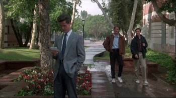 Movie still from “Gross Anatomy” (1989), directed by Thom Eberhardt – A man in a suit and tie standing next to a tree; Wide shot, Low angle