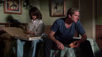 Movie still from “Gross Anatomy” (1989), directed by Thom Eberhardt – A man and a woman sitting on a couch eating pizza; Medium shot, High angle
