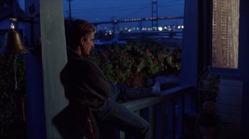 Movie still from “Gross Anatomy” (1989), directed by Thom Eberhardt – A man sitting on a porch looking out at a bridge at night; Wide shot, Over the shoulder angle