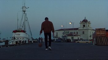 Movie still from “Gross Anatomy” (1989), directed by Thom Eberhardt – A man holding a basketball in a parking lot at night; Wide shot, Low angle