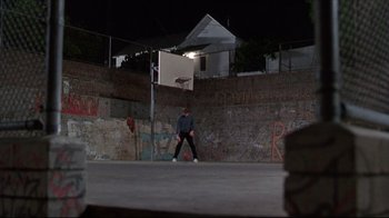 Movie still from “Gross Anatomy” (1989), directed by Thom Eberhardt – A man standing on a basketball court holding a ball; Wide shot, Low angle