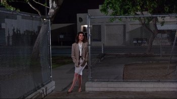Movie still from “Gross Anatomy” (1989), directed by Thom Eberhardt – A woman standing in front of a chain link fence at night; Wide shot, Low angle
