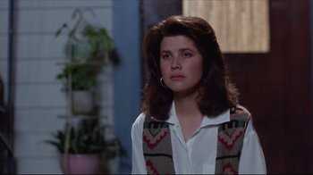 Movie still from “Gross Anatomy” (1989), directed by Thom Eberhardt – A young woman with long brown hair wearing a white shirt and a vest; Close Up shot, Over the shoulder angle