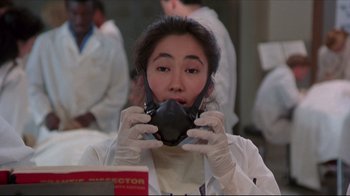 Movie still from “Gross Anatomy” (1989), directed by Thom Eberhardt – A woman in a white lab coat holding up a gas mask to her face; Close Up shot, Low angle