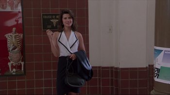 Movie still from “Gross Anatomy” (1989), directed by Thom Eberhardt – A young woman holding a purse in front of a brick wall; Medium shot, Low angle
