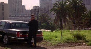 Movie still from “Grosse Pointe Blank” (1997), directed by George Armitage – A man standing in front of a parked car; Wide shot, Low angle