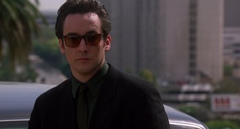 Movie still from “Grosse Pointe Blank” (1997), directed by George Armitage – A person wearing a suit and sunglasses; Close Up shot, Low angle