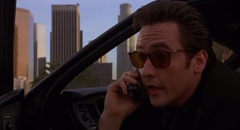 Movie still from “Grosse Pointe Blank” (1997), directed by George Armitage – A man talking on a cell phone while sitting in a car; Close Up shot, Low angle