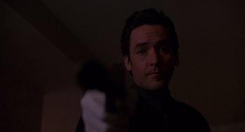 Movie still from “Grosse Pointe Blank” (1997), directed by George Armitage – A man holding a gun in a dark room; Close Up shot, Low angle