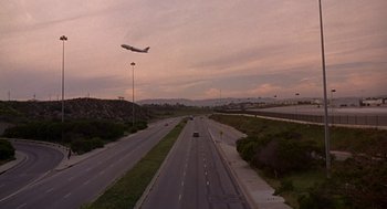 Movie still from “Grosse Pointe Blank” (1997), directed by George Armitage – An airplane is flying over an empty highway; Extreme Wide shot, Low angle