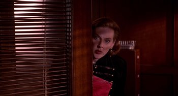 Movie still from “Grosse Pointe Blank” (1997), directed by George Armitage – A woman is peeking through the blinds of a window; Medium shot, Over the shoulder angle