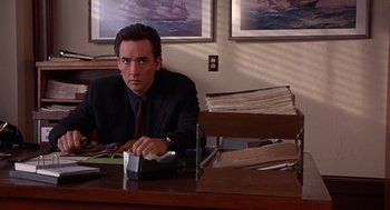 Movie still from “Grosse Pointe Blank” (1997), directed by George Armitage – A man sitting at a desk in front of papers; Medium shot, Low angle