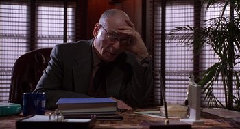 Movie still from “Grosse Pointe Blank” (1997), directed by George Armitage – An older man sitting at a table with a book; Medium shot, Low angle
