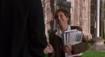 Movie still from “Grosse Pointe Blank” (1997), directed by George Armitage – A woman is holding a stack of newspapers and smiling; Medium shot, Over the shoulder angle