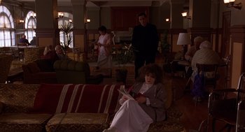 Movie still from “Grosse Pointe Blank” (1997), directed by George Armitage – A woman sitting on a couch in a living room; Wide shot, High angle