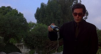 Movie still from “Grosse Pointe Blank” (1997), directed by George Armitage – A man in a black suit and sunglasses holding a bottle; Medium shot, Low angle