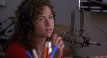 Movie still from “Grosse Pointe Blank” (1997), directed by George Armitage – A woman with curly hair wearing headphones and holding a pencil in her hand; Close Up shot, High angle