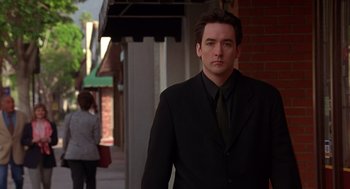 Movie still from “Grosse Pointe Blank” (1997), directed by George Armitage – A man wearing a suit and tie standing in front of a building; Medium shot, Low angle