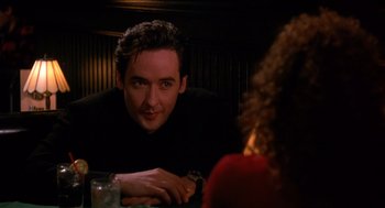 Movie still from “Grosse Pointe Blank” (1997), directed by George Armitage – A man sitting at a table in front of a woman; Close Up shot, Over the shoulder angle