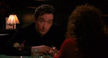 Movie still from “Grosse Pointe Blank” (1997), directed by George Armitage – A man sitting at a table in front of a woman; Close Up shot, Over the shoulder angle