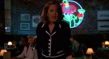 Movie still from “Grosse Pointe Blank” (1997), directed by George Armitage – A woman in a black and white jacket is holding a drink; Medium shot, Over the shoulder angle