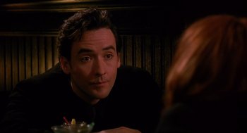 Movie still from “Grosse Pointe Blank” (1997), directed by George Armitage – A person sitting at a table; Close Up shot, Over the shoulder angle