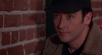 Movie still from “Grosse Pointe Blank” (1997), directed by George Armitage – A person wearing a hat near a brick wall; Close Up shot, High angle