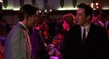 Movie still from “Grosse Pointe Blank” (1997), directed by George Armitage – A group of men and women in suits and ties talking to each other in a room; Medium shot, Over the shoulder angle
