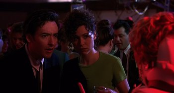 Movie still from “Grosse Pointe Blank” (1997), directed by George Armitage – A man and a woman standing next to each other in a room; Close Up shot, Over the shoulder angle