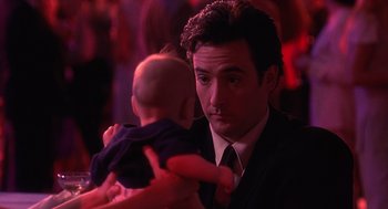 Movie still from “Grosse Pointe Blank” (1997), directed by George Armitage – A man in a suit and tie holding a baby in his arms; Close Up shot, Over the shoulder angle