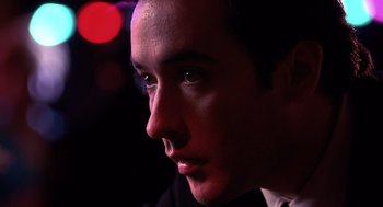 Movie still from “Grosse Pointe Blank” (1997), directed by George Armitage – A man's face in the dark; Close Up shot, Over the shoulder angle