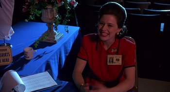 Movie still from “Grosse Pointe Blank” (1997), directed by George Armitage – A woman sitting at a table smiling for the camera; Medium shot, Over the shoulder angle