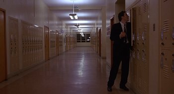 Movie still from “Grosse Pointe Blank” (1997), directed by George Armitage – A man in a suit standing in the hallway of a school; Wide shot, Low angle