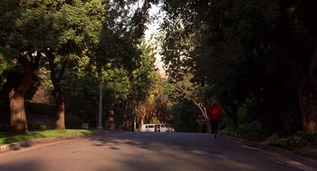 Movie still from “Grosse Pointe Blank” (1997), directed by George Armitage – A white suv driving down a street next to a forest; Extreme Wide shot, Low angle