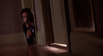 Movie still from “Grosse Pointe Blank” (1997), directed by George Armitage – A man in a suit and tie pointing a gun at a door; Medium shot, Low angle