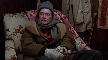 Movie still from “Grumpy Old Men” (1993), directed by Donald Petrie – An older man sitting on a couch holding a cigarette; Medium shot, High angle