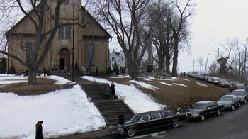 Movie still from “Grumpy Old Men” (1993), directed by Donald Petrie – A car parked on the side of the road next to a church; Extreme Wide shot, High angle