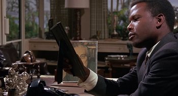 Movie still from “Guess Who's Coming to Dinner” (1967), directed by Stanley Kramer – A man sitting at a table holding a book in front of him; Close Up shot, Low angle