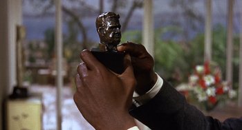 Movie still from “Guess Who's Coming to Dinner” (1967), directed by Stanley Kramer – A person holding a statue of a man in front of a building; Extreme Close Up shot, Low angle