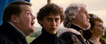 Movie still from “Gulliver's Travels” (2010), directed by Rob Letterman – A young man with curly brown hair standing next to two older men; Close Up shot, Over the shoulder angle