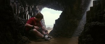 Movie still from “Gulliver's Travels” (2010), directed by Rob Letterman – A man sitting in front of an opening in a cave; Wide shot, Low angle