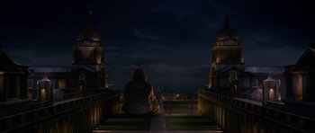 Movie still from “Gulliver's Travels” (2010), directed by Rob Letterman – A person sitting on the ground in front of a building at night; Extreme Wide shot, High angle