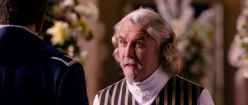 Movie still from “Gulliver's Travels” (2010), directed by Rob Letterman – An older man with long white hair wearing a striped vest; Close Up shot, Over the shoulder angle