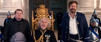 Movie still from “Gulliver's Travels” (2010), directed by Rob Letterman – An old man in a black suit sitting on a gold chair; Medium shot, Low angle